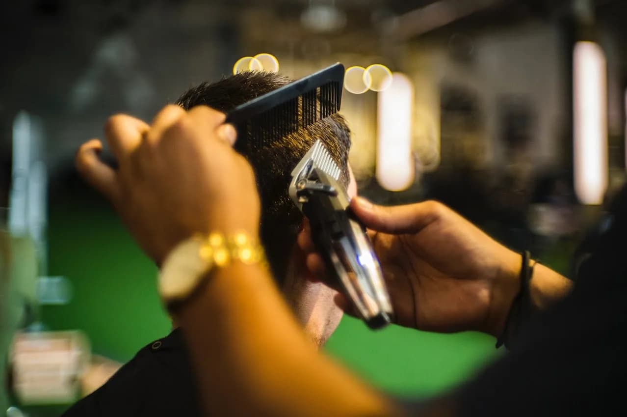 Close-up of Dre guiding clippers along a comb to refine a haircut